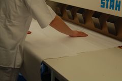 Zwei Hände legen eine Tischdecke auf eine große Bügelmaschine.